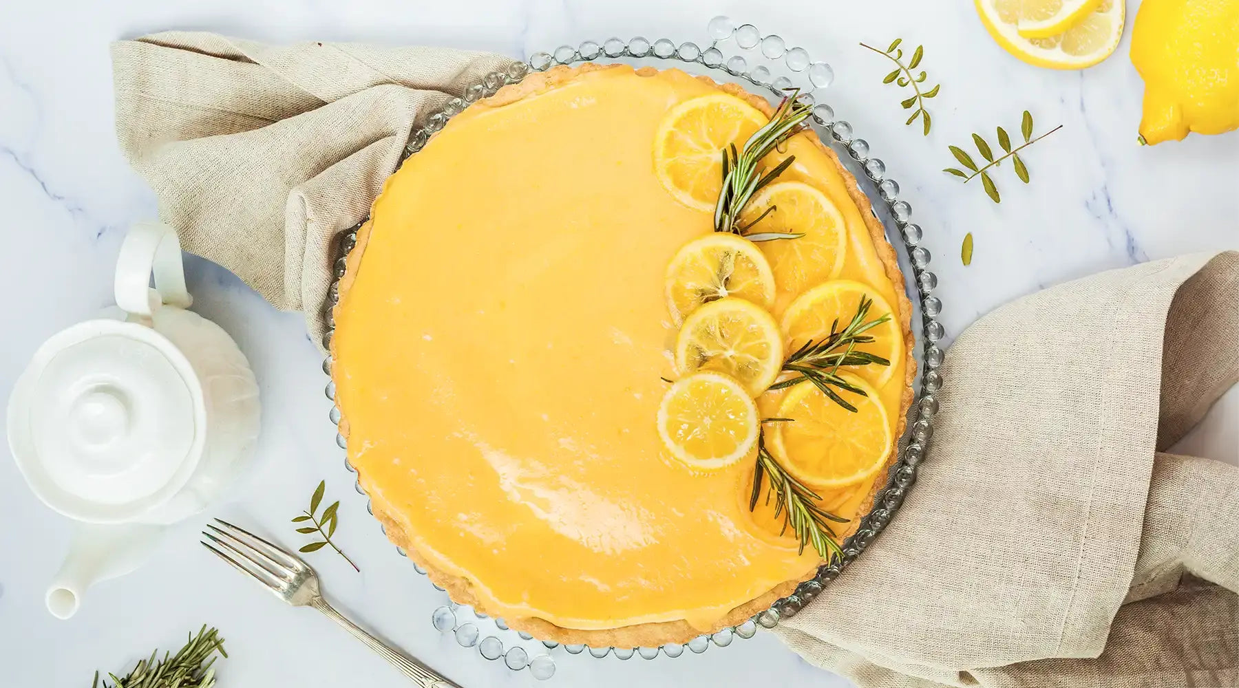 Zitronentarte nach dem Rezept von Oma Barbara von Kuchentratsch, dekoriert mit Zitronenscheiben und Rosmarinzweigen auf einer Kuchenplatte