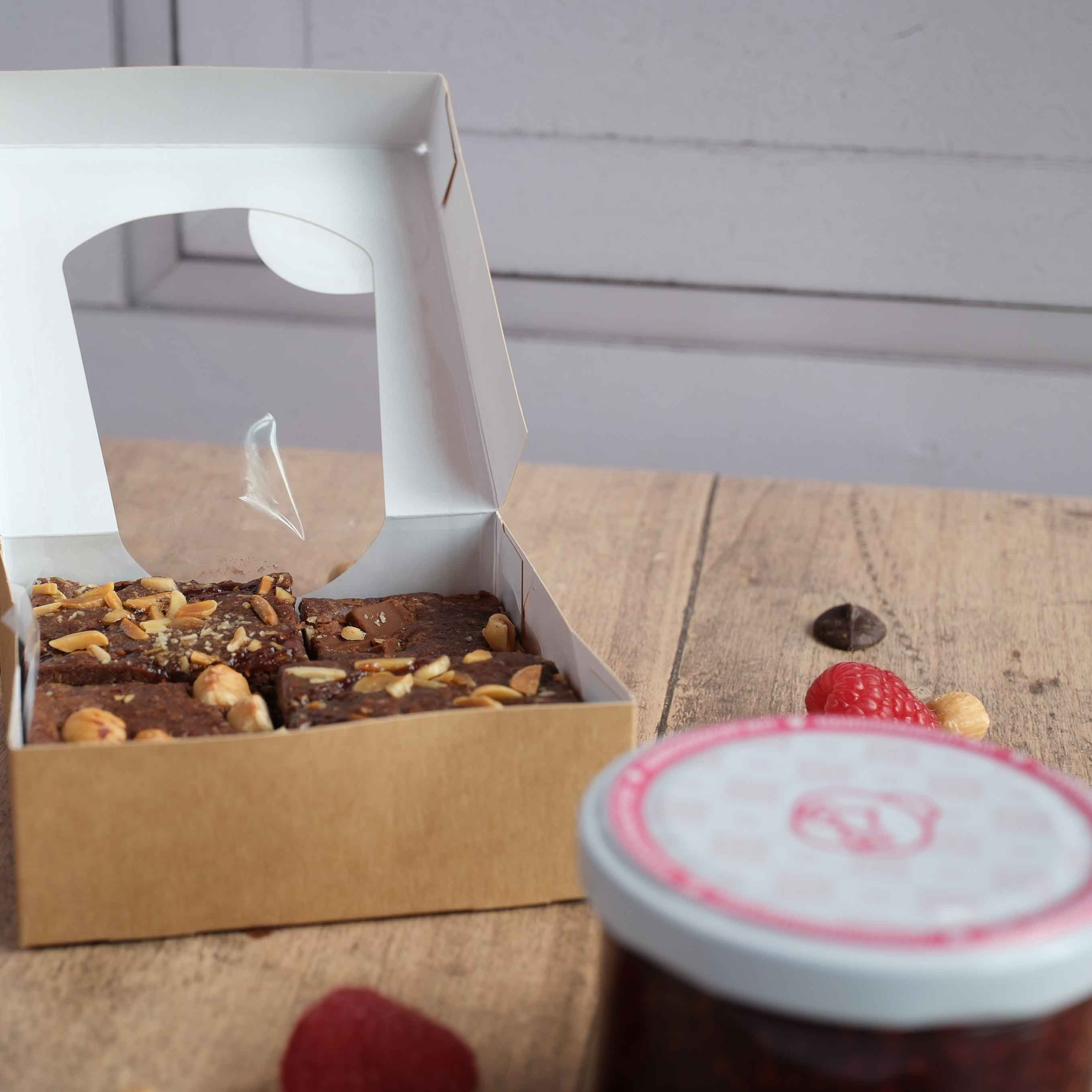Die Brownies von Oma Brigitte im 4er Set in den Sorten Himbeere und Haselnuss auf Holztisch in ihrem Versandkarton