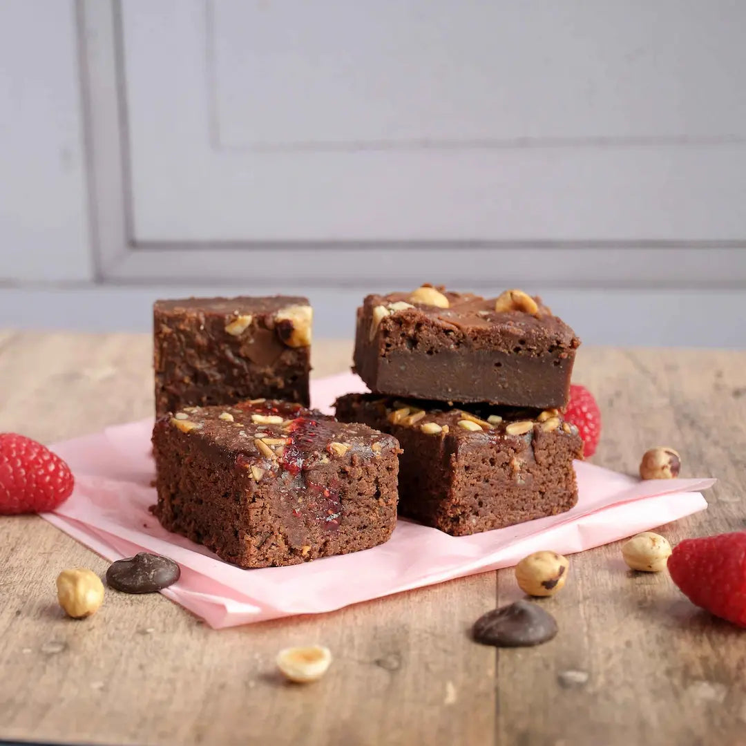 Die Brownies von Oma Brigitte im 4er Set in den Sorten Himbeere und Haselnuss auf Holztisch und rosa Serviette