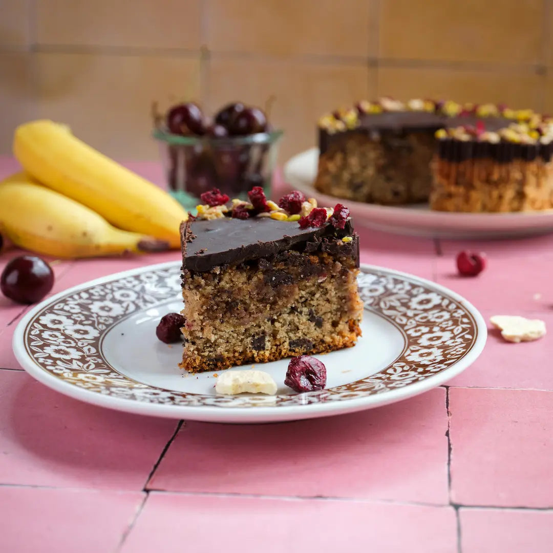 Unser Banane-Kirsch-Kuchen x buah von Kuchentratsch. Ein Stück mit dem Kuchem im Hintergrund.