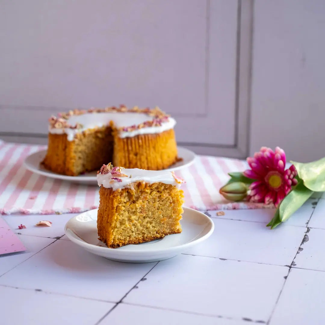 Karottenkuchen von Oma Irmgard von Kuchentratsch. Ein Stück mit dem ganzen Kuchen im Hintergrund.