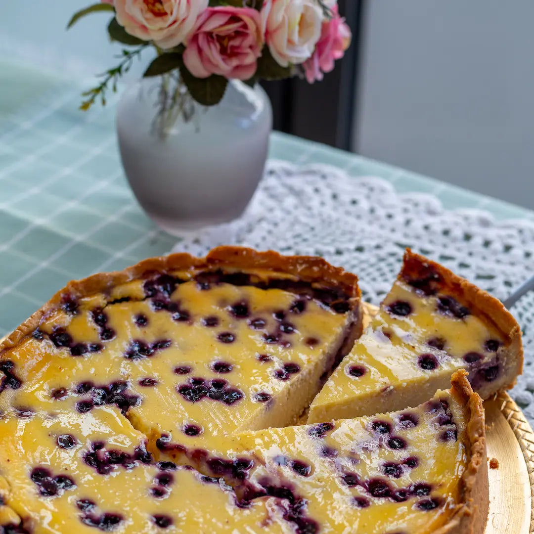 Der Käsekuchen mit Heidelbeeren von Oma Anna auf einem Tisch mit Blumen im Hintergrund
