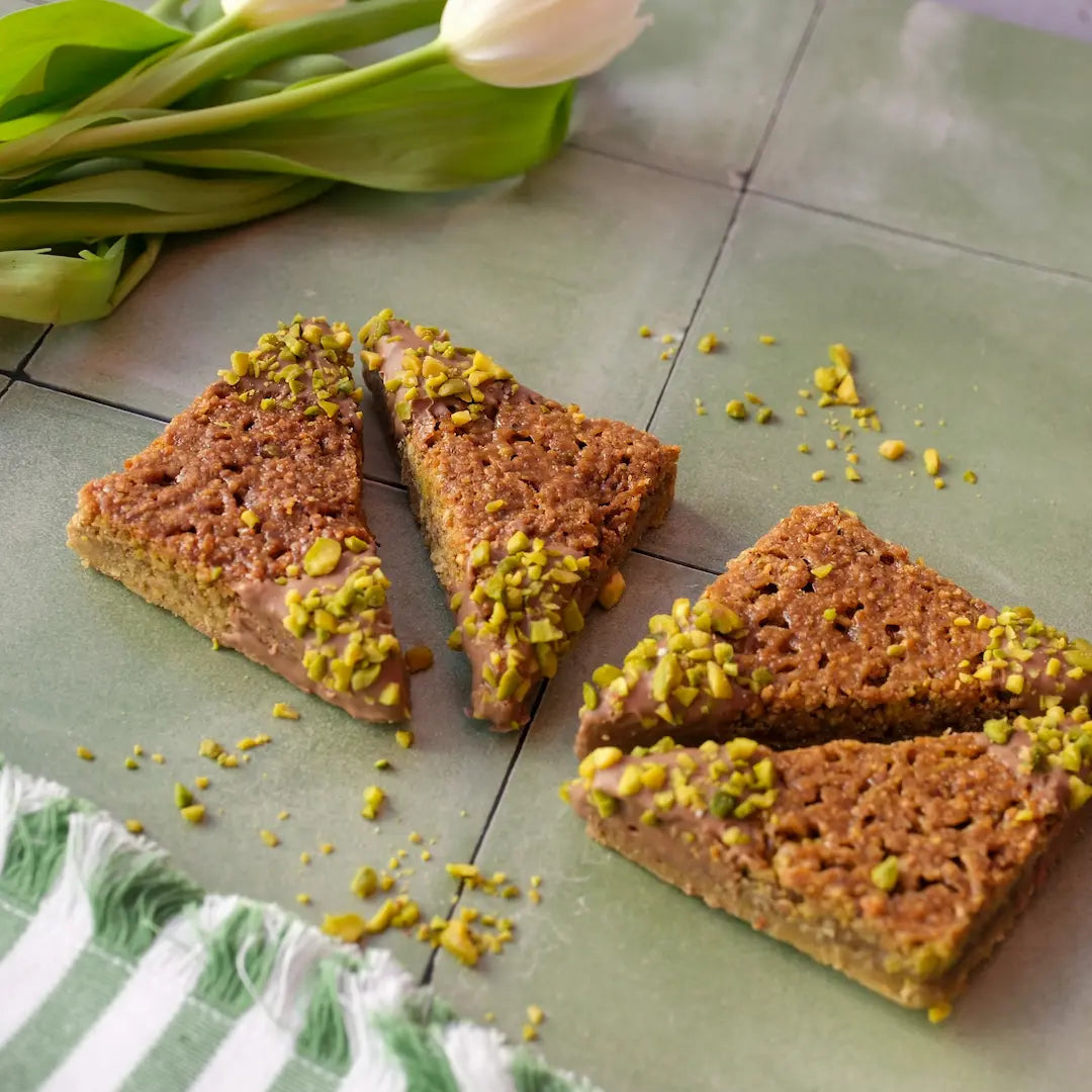 Vier Stück der Pistazienecken von den Kuchentratsch Omas auf grünen Fließen mit weißen Tulpen und Pistazien.
