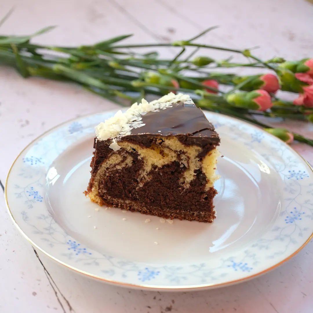 Ein Stück von Oma Connys Marmor-Kuchen von Kuchentratsch mit Blumen im Hintergrund