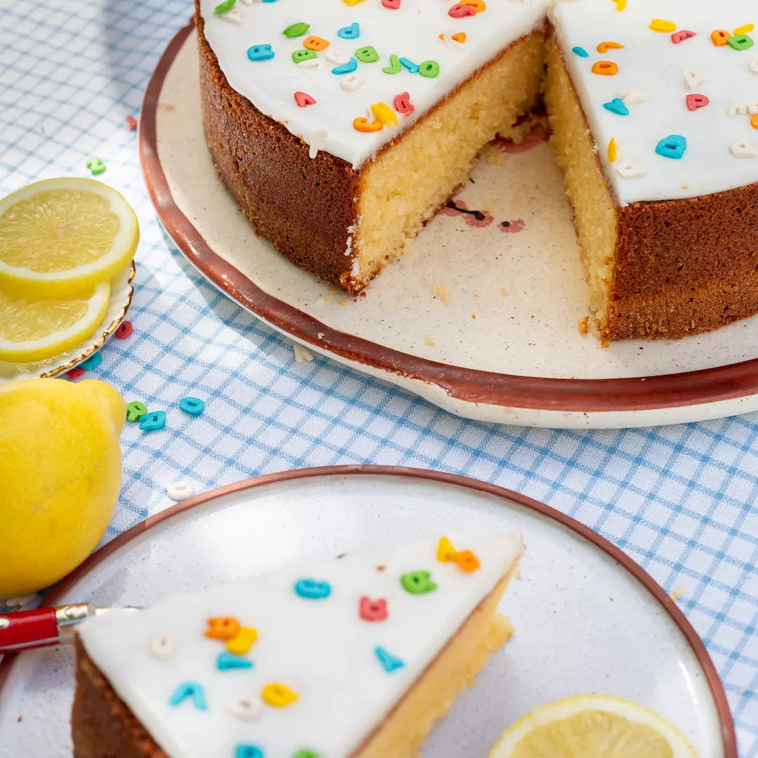 Einschulungs-Zitronenkuchen von Oma Helga Groß mit Buchstabendeko angeschnitten. Ein einzelnes Stück im Vordergrund. 