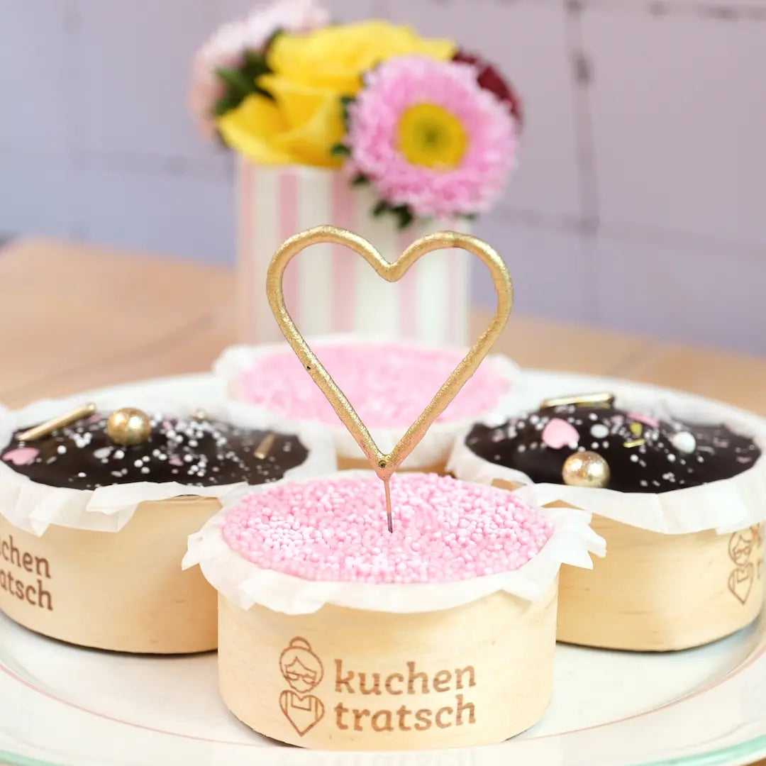 Vier Geburtstagsmuffins von oben fotografiert: zwei mit rosa Streuseln und zwei mit Schokoglasur, angerichtet auf einem weißen Teller.