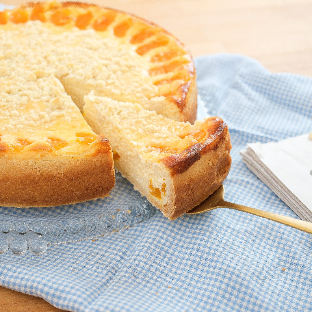 Mandarine Schmand Kuchen von Kuchentratsch seitlich  fotografiert, ein Stück herausgeschnitten