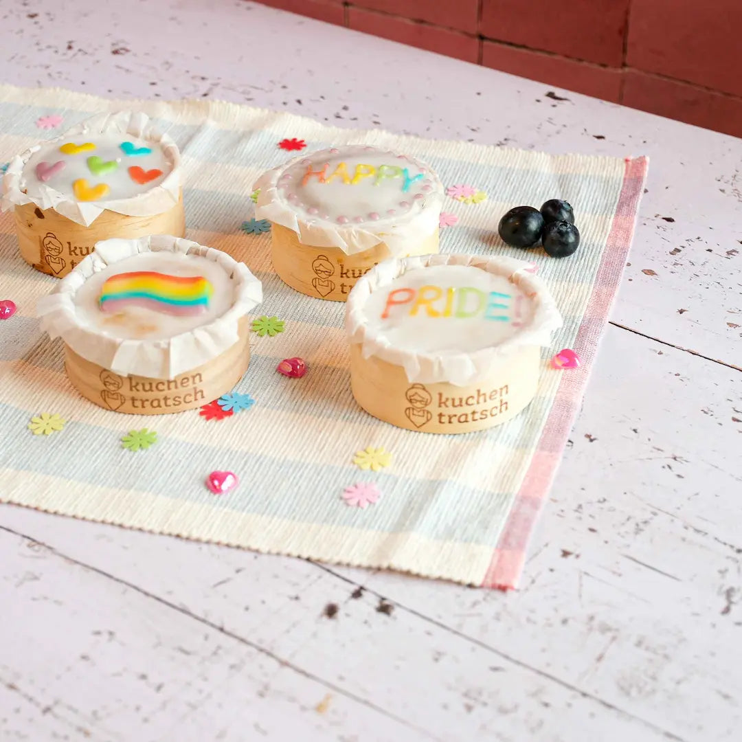 Das Kuchentratsch Muffin Set im Happy Pride Look auf Tisch mit Konfetti und Heidelbeeren 