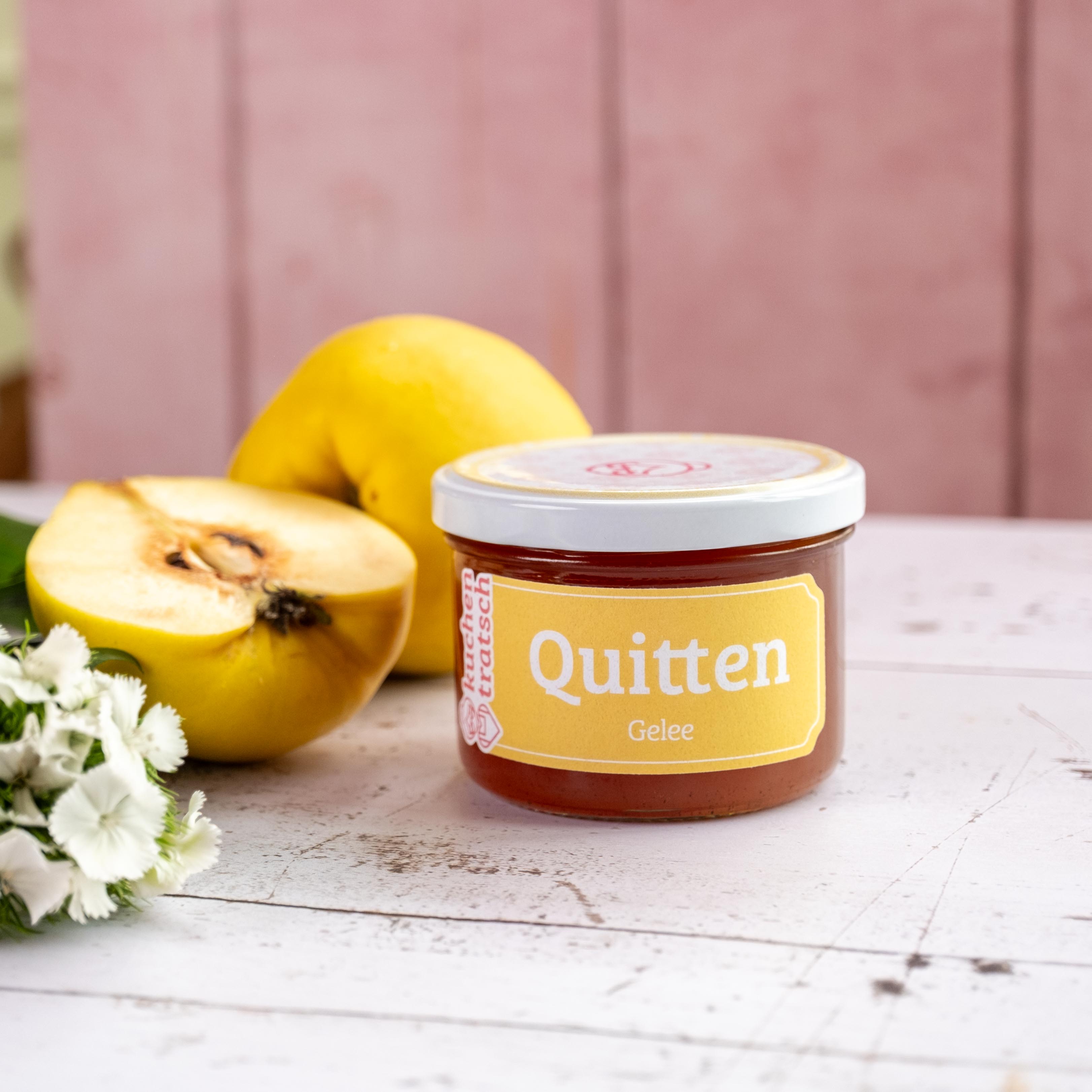 Quittengelee von Kuchentratsch auf weißem Tisch mit Blumen und frischen Quitten