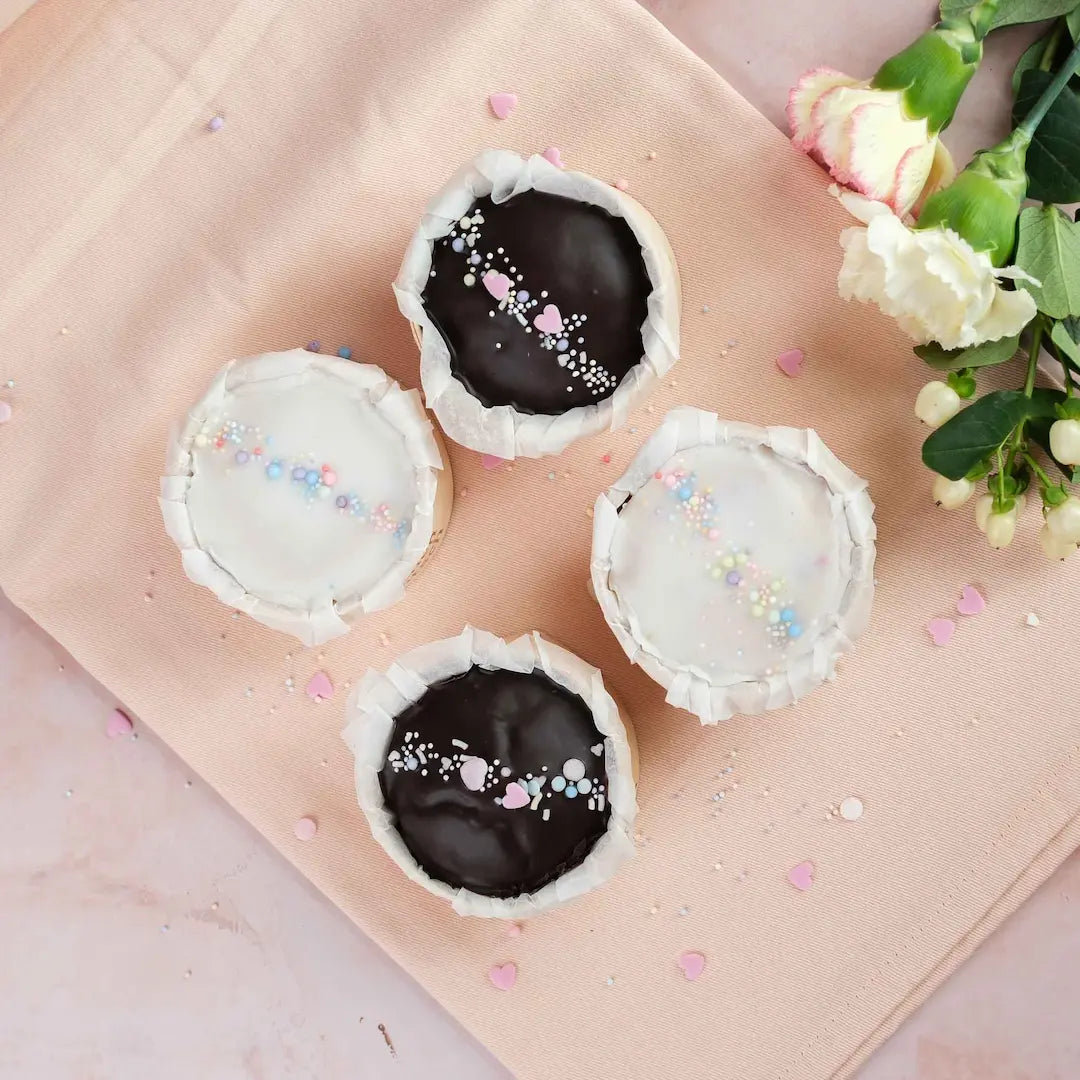 Törtchenliebe von Kuchentratsch fotografiert von oben auf rosa Tischdecke mit Streuseln und Blumen 