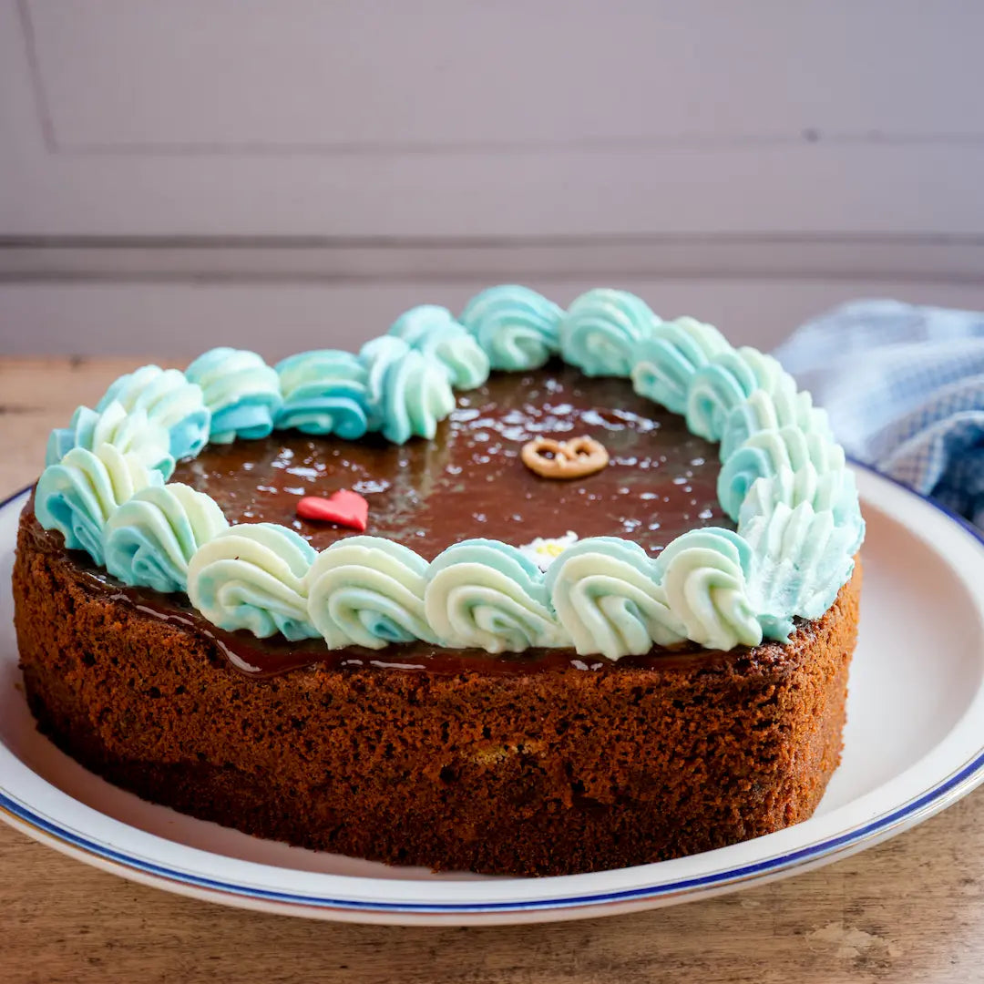 Saftiger Nusskuchen mit Amaretto im Anschnitt, sichtbar mit Aprikosenmarmelade bestrichen und blau-weißem Frischkäse-Frosting dekoriert.