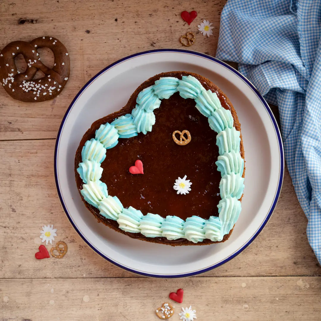 Nusskuchen mit Amaretto von Kuchentratsch in der Wiesn-Edition, bestrichen mit Aprikosenmarmelade, blau-weißem Frischkäse-Topping und süßer Zuckerdeko in Herzform.