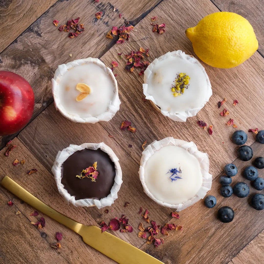 Vegane Muffins von Kuchentratsch in vier verschiedenen Sorten mit Früchten auf einem Tisch fotografiert von oben mit Blütendeko